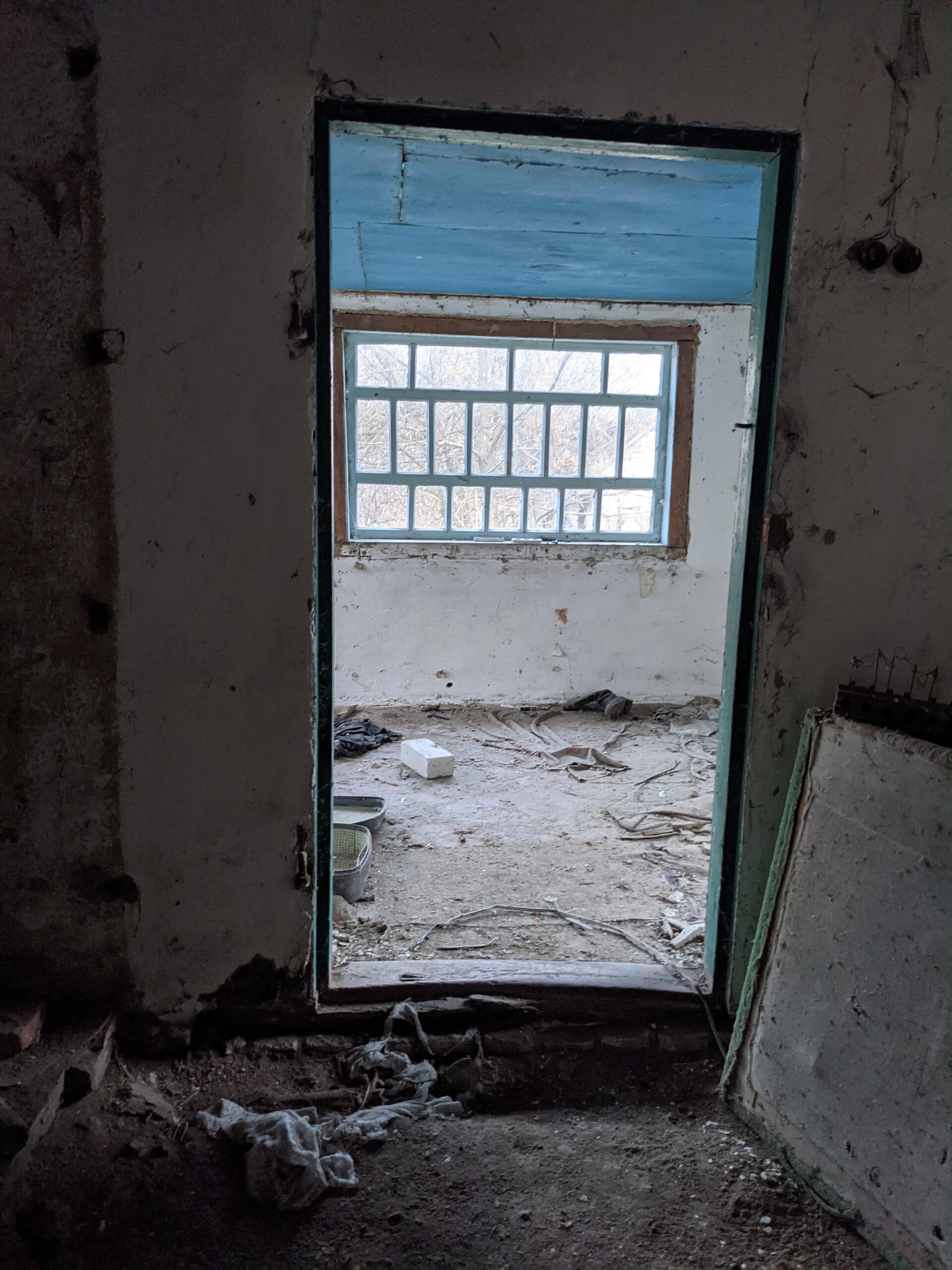 Empty door frame opening onto a window in a dilapidated, abandoned dwelling